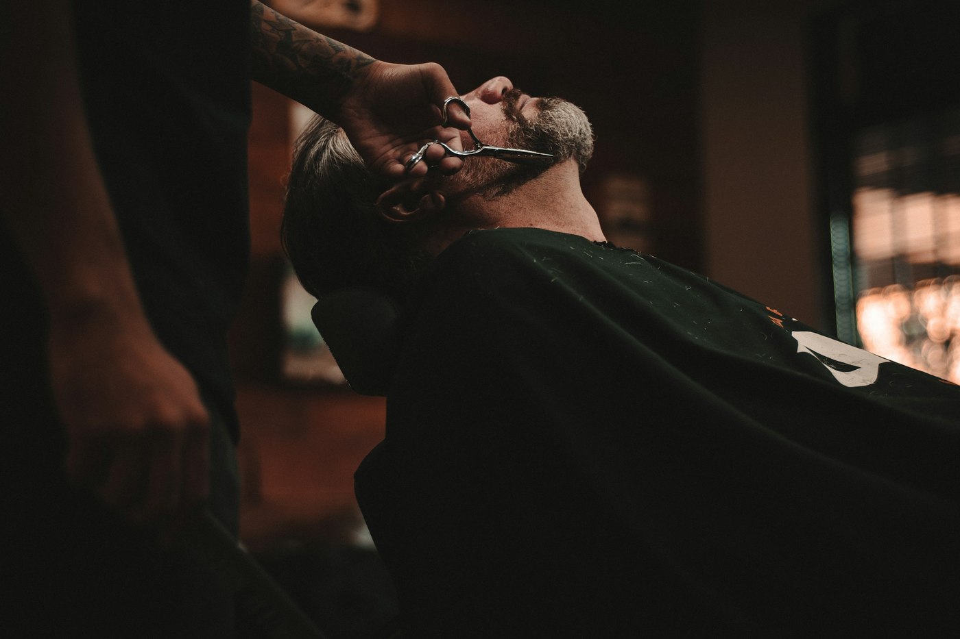 A barber working on a reclined customer, the shop dark behind them